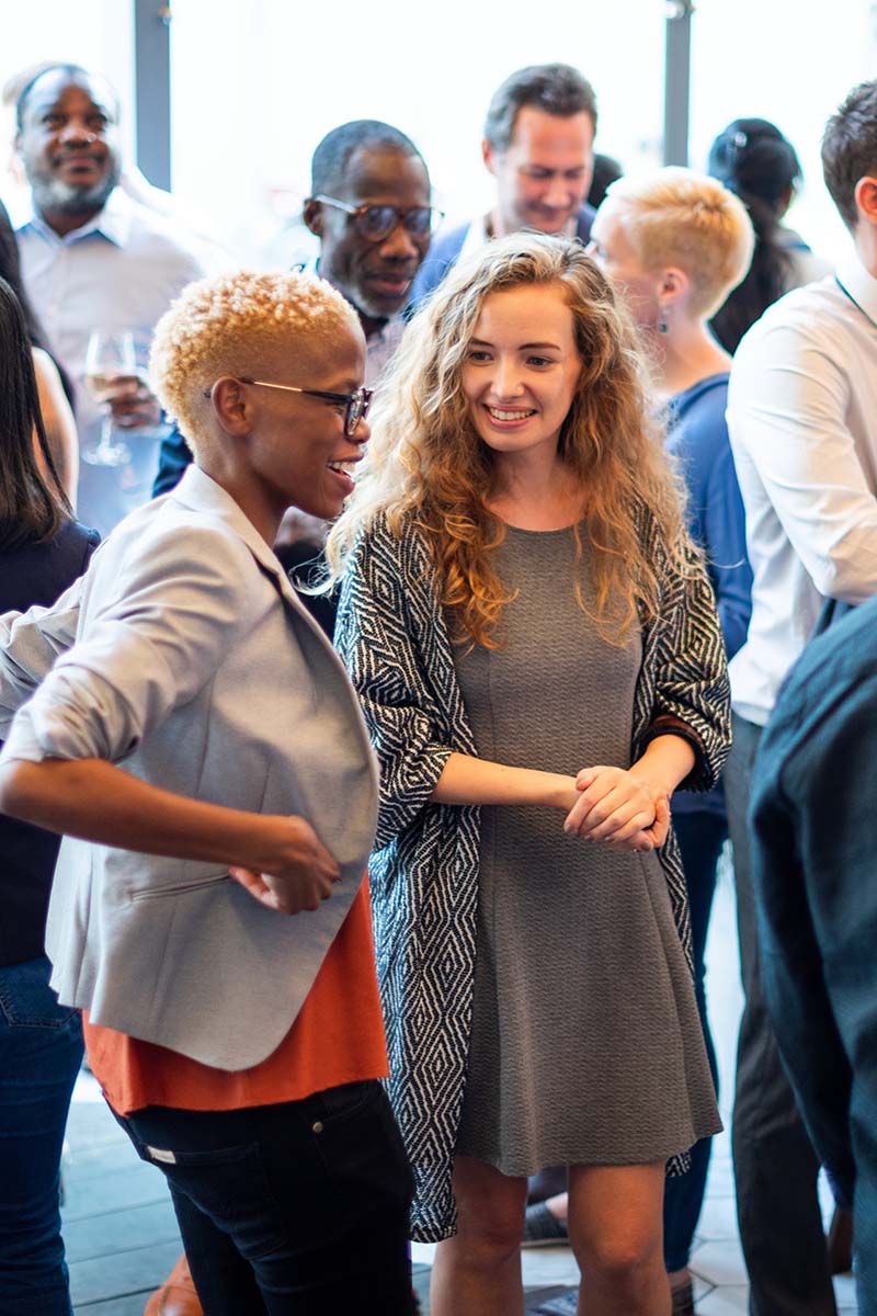 Associations header 800x1200px Diverse group socializing at an association event. Men and women of various ethnicities engaged in conversation. Lively atmosphere with diverse attendees. Diverse people mingle at a social event.