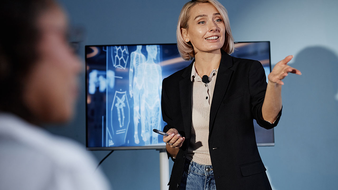 Extended Learning 1280x720px female presenting in front of monitor with human visual