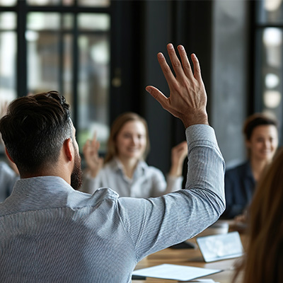 Hard Question 400x400px man in meeting with his hand raised to ask a question