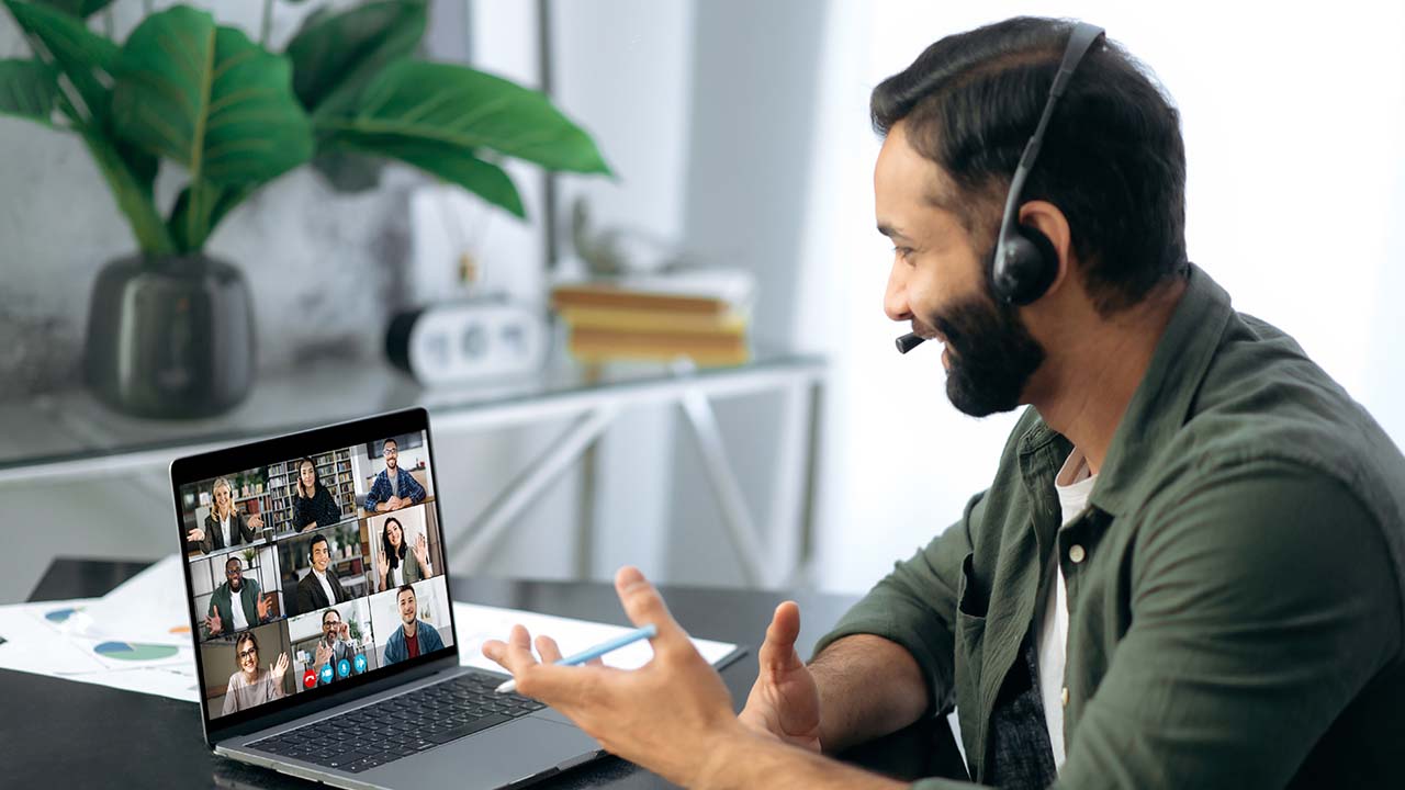 Leadership Briefing 1280x720px bearded male with headset on giving a leadership briefing to a group of fellow workers who are online. he is looking at the screen which shows multiple people in attendence