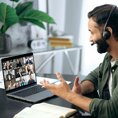 Leadership Briefing mobile 400x400px bearded male with headset on giving a leadership briefing to a group of fellow workers who are online. he is looking at the screen which shows multiple people in attendence