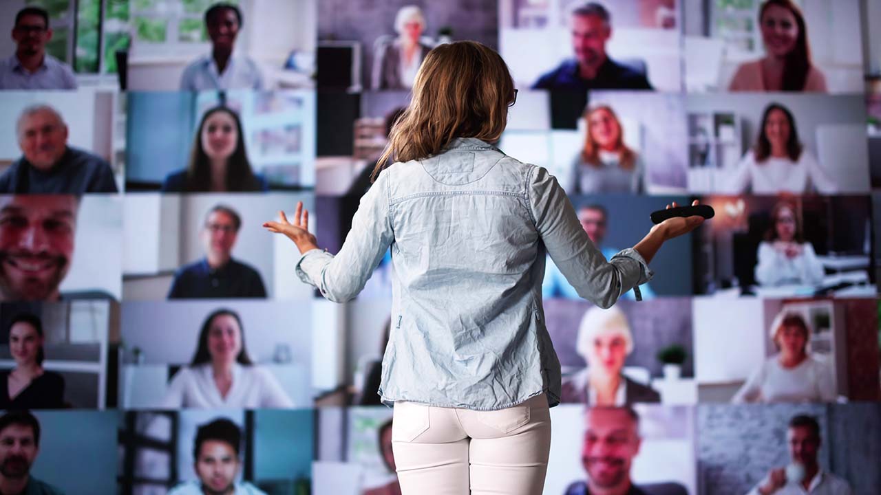 Live Events 1280x720px Lady standing presenting in front of a mulitiple screen of attendess