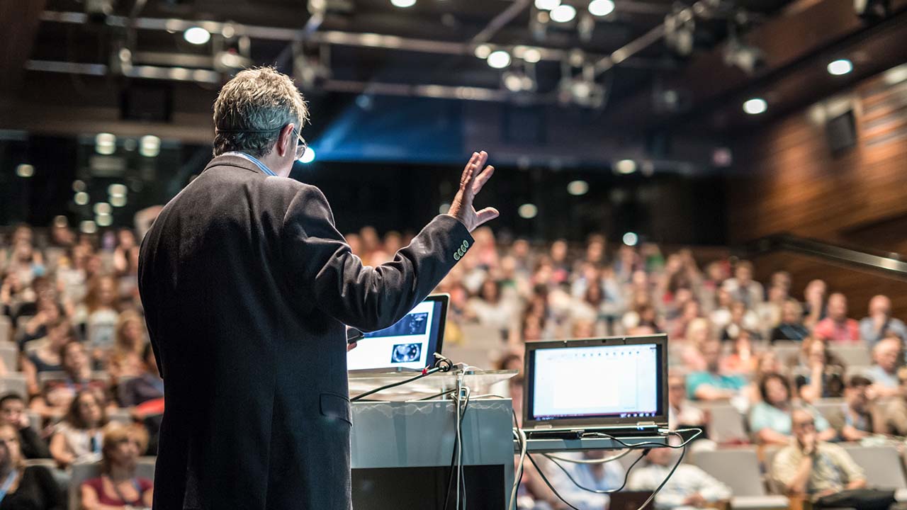 Partner programs 1280x720px Male presenter on stage presenting to a cohort of students in lecture theatre which is also being broadcast to online students