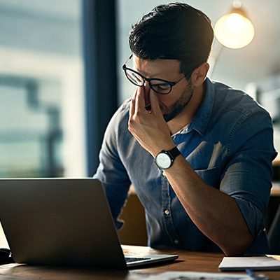 Young male professional at desk in front of laptop seeming to be frustrated with work